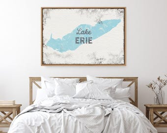 May include: A rectangular wall art piece in a light wood frame featuring a distressed white background with a light blue map of Lake Erie. The text Lake ERIE is printed in a dark gray font in the center of the blue lake illustration.