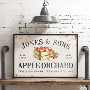 a framed sign for Jones & Sons Apple Orchard, which is a family-owned and operated farm that has been in operation since 1946. The sign displays a picture of a wooden crate filled with apples, indicating that the orchard produces and sells apples. The sign is hanging on a wall, and there is a light fixture above it.