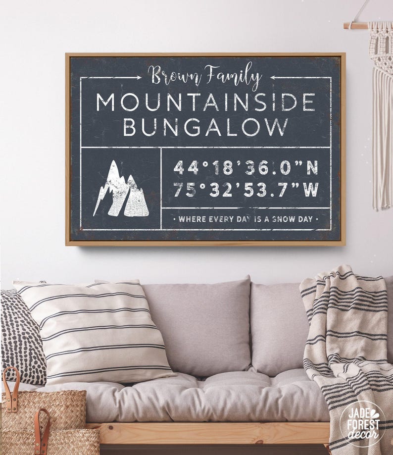 a framed sign with the text "Brown Family MOUNTAINSIDE BUNGALOW" and a mountain icon, mounted on a wall above a couch with a striped blanket draped over it.