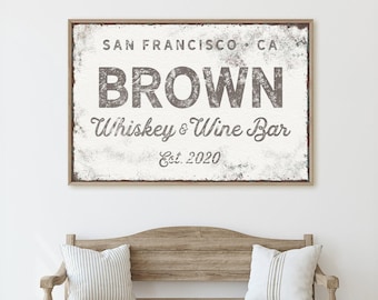 May include: A rectangular wall sign with a distressed white background and a thin wooden frame. The text reads SAN FRANCISCO CA, BROWN, Whiskey & Wine Bar, and Est. 2020 in dark gray, weathered lettering. The sign has a rustic, aged appearance.