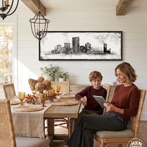 A woman and a young boy are seated at a wooden dining table, with a framed cityscape artwork hanging on the wall above them. The woman is using a tablet, while the boy is looking at the screen. The table is set with various glassware, including wine glasses and cups, and there are potted plants and vases on the table.
