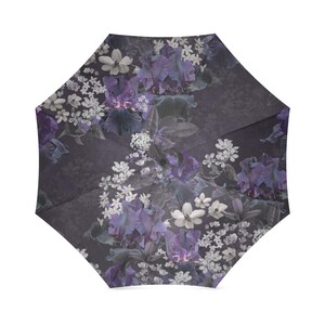May include: A purple and white floral print umbrella with a dark gray background. The umbrella is closed and the floral pattern is visible on the outside.