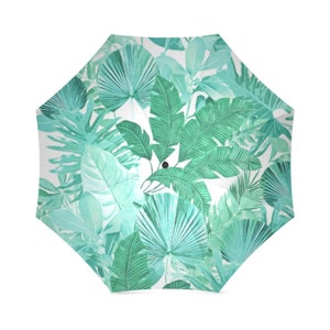 May include: A green and white umbrella with a tropical leaf pattern. The umbrella is closed and has a black handle.