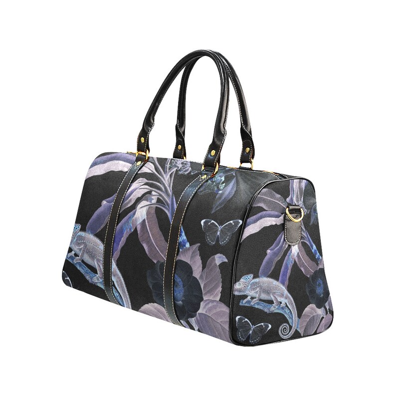 May include: Black travel bag with a floral print featuring purple and blue flowers, butterflies, and chameleons. The bag has black leather accents and gold hardware.