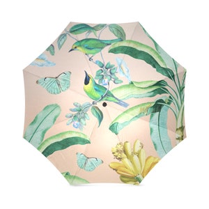 May include: A beige umbrella with a tropical print featuring green leaves, yellow bananas, green and blue butterflies, and green birds.