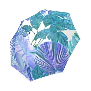 May include: A white umbrella with a tropical leaf pattern in shades of blue and green. The leaves are stylized and have a watercolor effect.