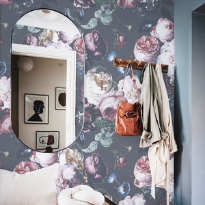 May include: Dark gray wallpaper featuring a large-scale floral pattern with pink, purple, and white roses and blue morning glories. The scene includes a wooden bench with a cream cushion, a brown leather bag, a light jacket, and a tall mirror.