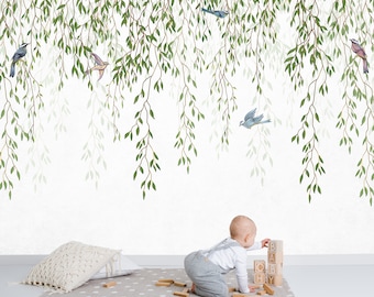 May include: A wall mural featuring hanging green willow branches and various small birds in flight and perched. A child in grey overalls and a white shirt plays with wooden blocks spelling BABY on a grey polka dot rug with a white textured pillow.