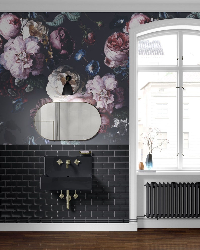 May include: A bathroom interior featuring dark floral wallpaper with large pink, purple, and blue blossoms. A black rectangular wall-mounted sink with gold-toned cross-handle faucets is centered above black subway tiles and below an oval mirror.