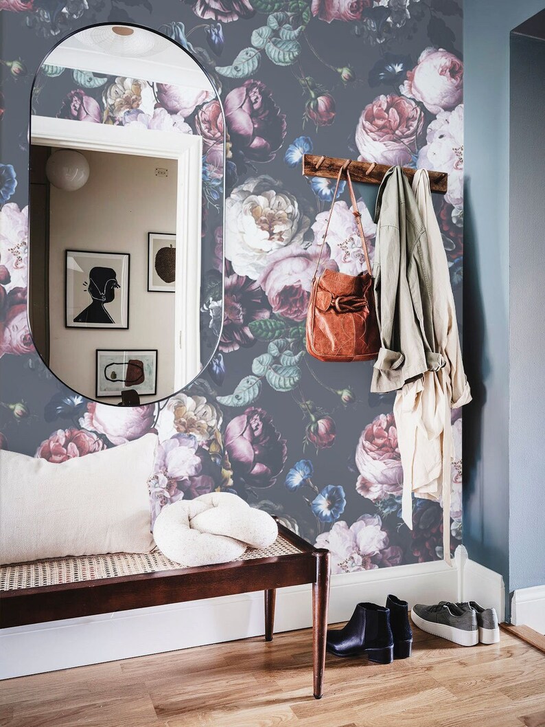 May include: Dark gray wallpaper featuring a large-scale floral pattern with pink, purple, and white roses and blue morning glories. The scene includes a wooden bench with a cream cushion, a brown leather bag, a light jacket, and a tall mirror.
