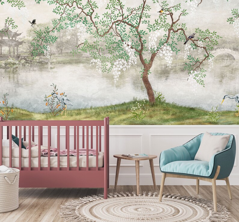 May include: A room interior featuring a dark pink cot, a light blue armchair with a white cushion, a small wooden side table, and a woven basket. The wall is covered in a mural depicting a landscape with a lake, a tree, and birds.