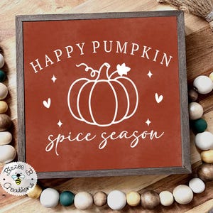 May include: A framed sign with a rust-colored background features white text that reads "HAPPY PUMPKIN spice season" with a pumpkin illustration. The sign is surrounded by a wooden frame and decorative beads.