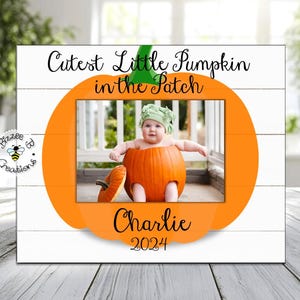May include: White wooden picture frame with a pumpkin-shaped cutout. The text "Cutest Little Pumpkin in the Patch" is written above the cutout. The cutout features a photo of a baby dressed as a pumpkin. The text "Charlie 2024" is written below the cutout.