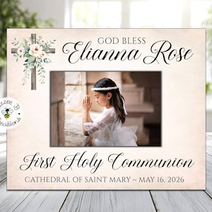 May include: A beige photo frame with the text "GOD BLESS Elianna Rose" and "First Holy Communion." A photo of a girl in a white dress is in the frame. A cross with floral accents is on the top left.