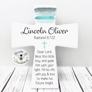 May include: White wooden cross with blue and gray watercolor paint. The cross has the name "Lincoln Oliver" and the text "Baptized 8.7.22". The cross also has a prayer that reads "Dear Lord, bless this little boy and guide him with your light. Fill his life with joy & love to make his future bright."