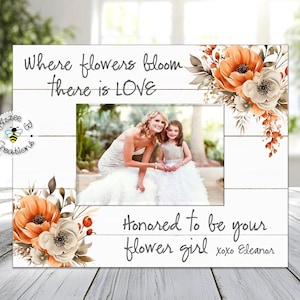 May include: A white wooden picture frame with a floral design and the text "Where flowers bloom there is LOVE" and "Honored to be your flower girl xoxo Eleanor". The frame has a photo of a bride and a flower girl.