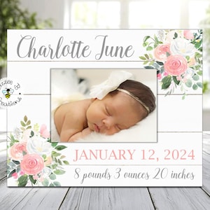 May include: A white picture frame with a floral design and a photo of a baby girl. The frame has the text "Charlotte June" at the top and "JANUARY 12, 2024 8 pounds 3 ounces 20 inches" at the bottom.