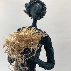 May include: A dark blue abstract sculpture of a person holding a bundle of natural fiber rope.