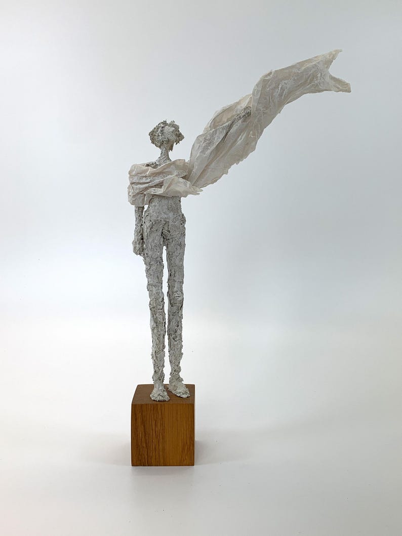 Vollansicht der off-white Skulptur einer menschlichen Figur auf einem quadratischen Eichenholzsockel mit einer stofflichen, wehenden Gewandform.