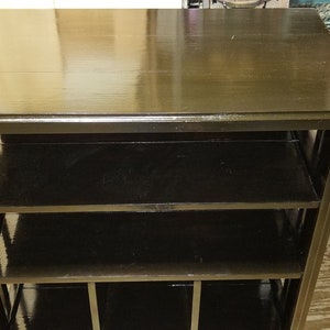 May include: A dark brown wooden shelf unit with four shelves. The shelves are open and have a grid pattern on the front.