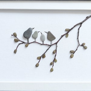 May include: A framed artwork featuring a twig with small brown pebbles arranged to look like leaves and gray pebbles arranged to look like birds perched on the twig.