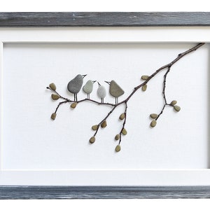 May include: A framed artwork featuring a pebble art design of four birds perched on a twig with leaves. The birds are gray and brown, and the leaves are green. The artwork is framed in a gray wood frame.
