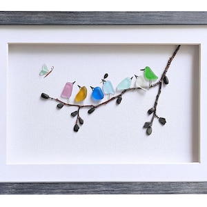 Op de afbeelding: Ingelijst kunstwerk met een tak met kleurrijke glazen vogels en een vlinder. De vogels zijn in roze, geel, blauw, lichtblauw, groen en wit. De lijst is grijs.