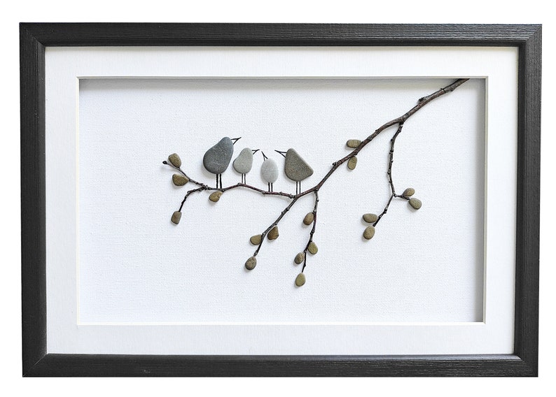 May include: A framed artwork featuring a pebble art design of four birds perched on a branch with leaves. The birds are gray and white, and the branch is brown. The artwork is set against a white background.