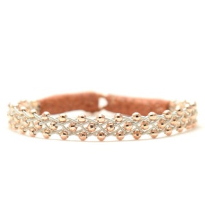 Könnte beinhalten: Ein geflochtenes Armband mit roségoldenen Perlen und einem Silberdrahtgeflecht.