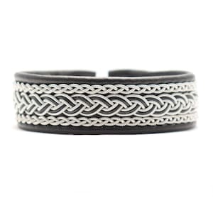 Könnte beinhalten: Ein schwarzes Lederarmband mit einem geflochtenen Silberdesign.