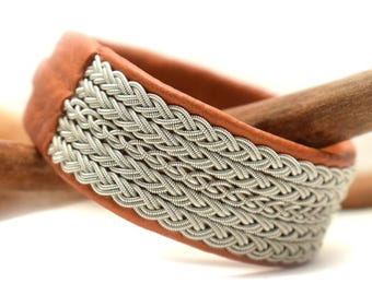 May include: A brown leather bracelet with a silver braided design. The bracelet is on a wooden surface.