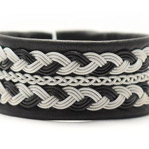 Könnte beinhalten: Ein schwarzes Lederarmband mit einem geflochtenen Silberdesign. Das Armband hat ein gewebtes Muster mit abwechselnden schwarzen und silbernen Strängen.