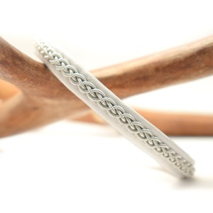 Könnte beinhalten: Ein weißes Lederarmband mit einem silbernen geflochtenen Besatz.
