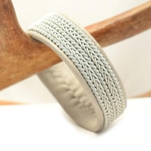 Könnte beinhalten: Ein weißes Lederarmband mit einem geflochtenen Silberdesign.