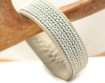 May include: A white leather bracelet with a silver braided design.