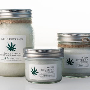 May include: Three glass jars with silver lids and brown twine tied around the top. The jars contain white wax and have labels that say "Weed Cover-Up" and "Bougie Candle for Dank Enthusiasts". The jars are 16 oz, 5 oz, and 4 oz.