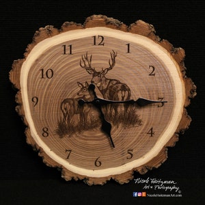 May include: A wooden clock with a rustic, natural bark edge. The clock face features a laser-engraved design of a buck and doe standing in a field of grass. The clock face is surrounded by Roman numeral hour markers.