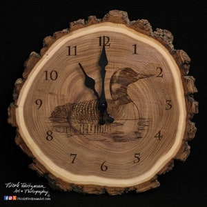 May include: A wooden clock with a loon design, featuring black hands and Roman numeral markings. The clock is made from a tree slice with the bark still attached.