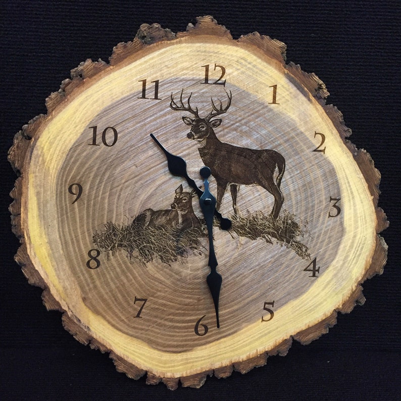 May include: A wooden clock with a rustic, tree bark design. The clock face features a laser-etched image of a buck and a fawn with Roman numeral hour markers. The clock hands are black.