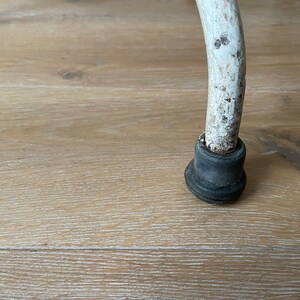 May include: Close-up of a white metal chair leg with a black rubber foot. The leg is slightly curved and has a worn, distressed finish.
