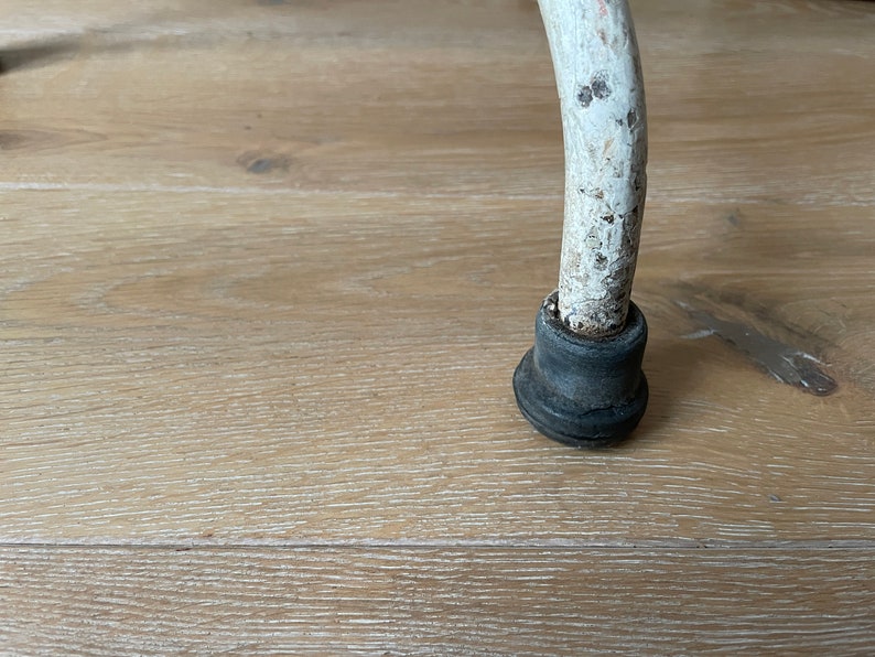 May include: Close-up of a white metal chair leg with a black rubber foot. The leg is slightly curved and has a worn, distressed finish.