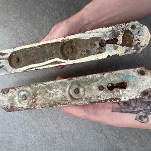 May include: Two antique metal door hardware pieces with keyholes and worn white paint. The pieces are rusty and have a distressed look.