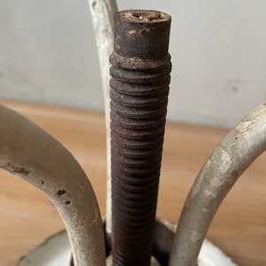 May include: Close-up of a white metal stool with a threaded metal rod and three legs. The rod is rusty and the legs are slightly chipped.