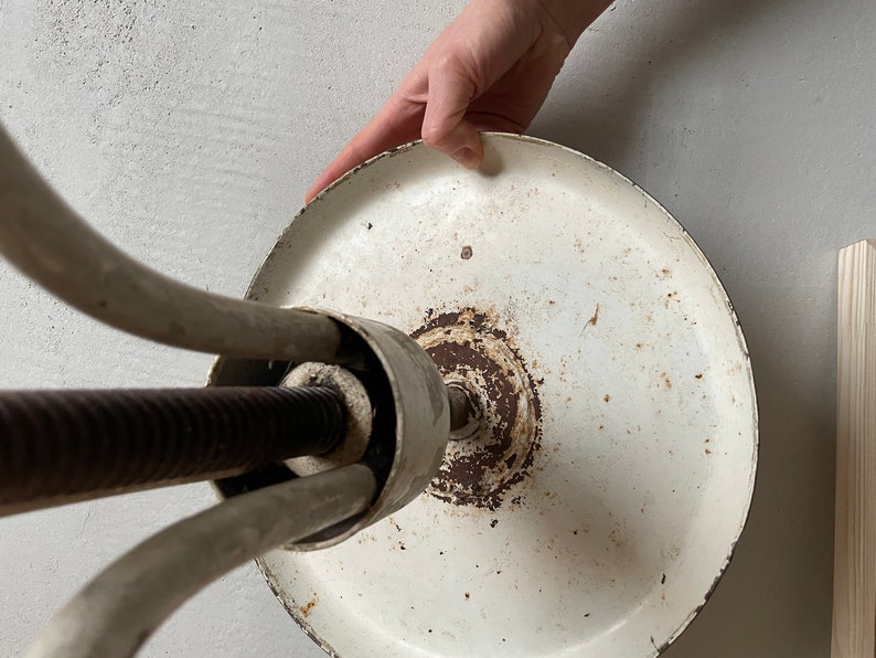 May include: White metal stool with a round base and three legs. The base is slightly rusted and the legs are adjustable.