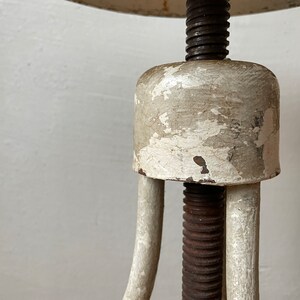 May include: A white metal adjustable stool with a round seat and a threaded metal rod. The stool has a worn, distressed finish.
