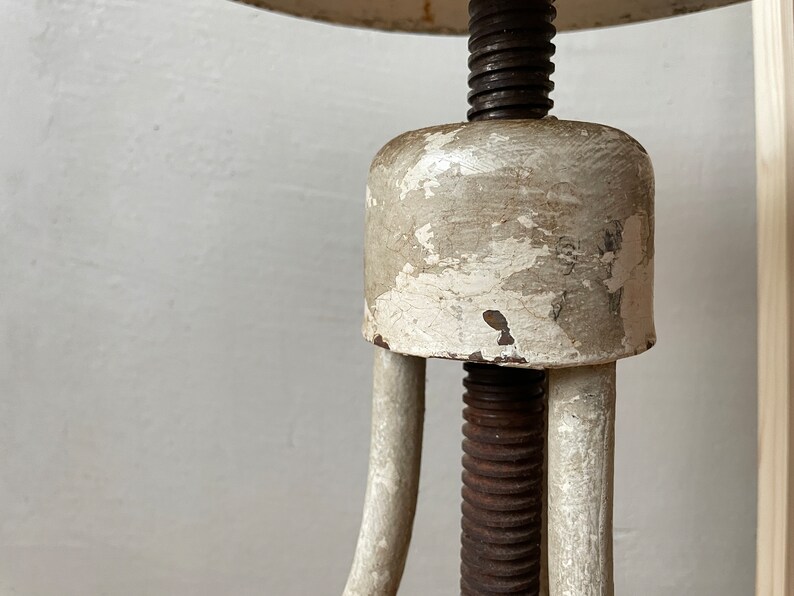 May include: A white metal adjustable stool with a round seat and a threaded metal rod. The stool has a worn, distressed finish.