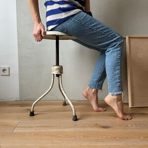 May include: A white metal adjustable stool with three legs. The stool has a round seat and a screw mechanism to adjust the height. The stool is in a room with wood floors.