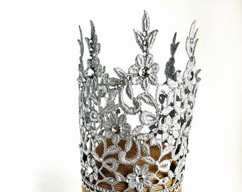 May include: A silver lace crown with rhinestones on a brown mannequin head.