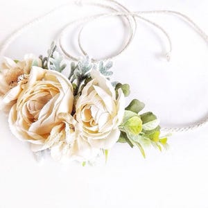 May include: A delicate floral crown with cream-colored roses and green leaves, tied with a natural twine cord.