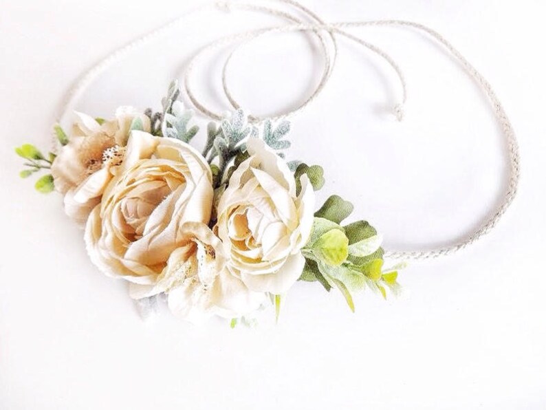 May include: A delicate floral crown with cream-colored roses and green leaves, tied with a natural twine cord.